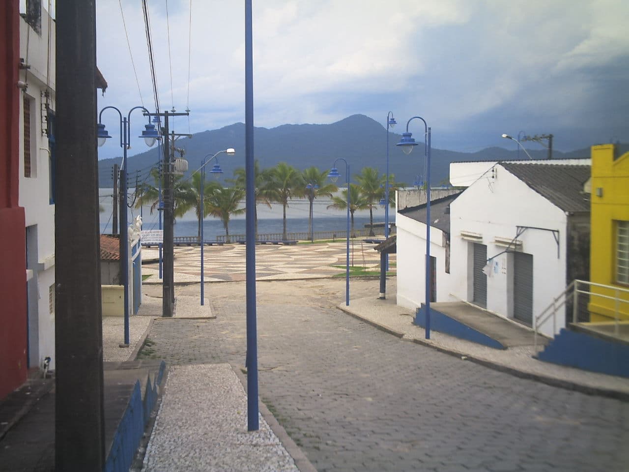 Rua histórica em declive com palmeiras, casario colonial e acesso à baía