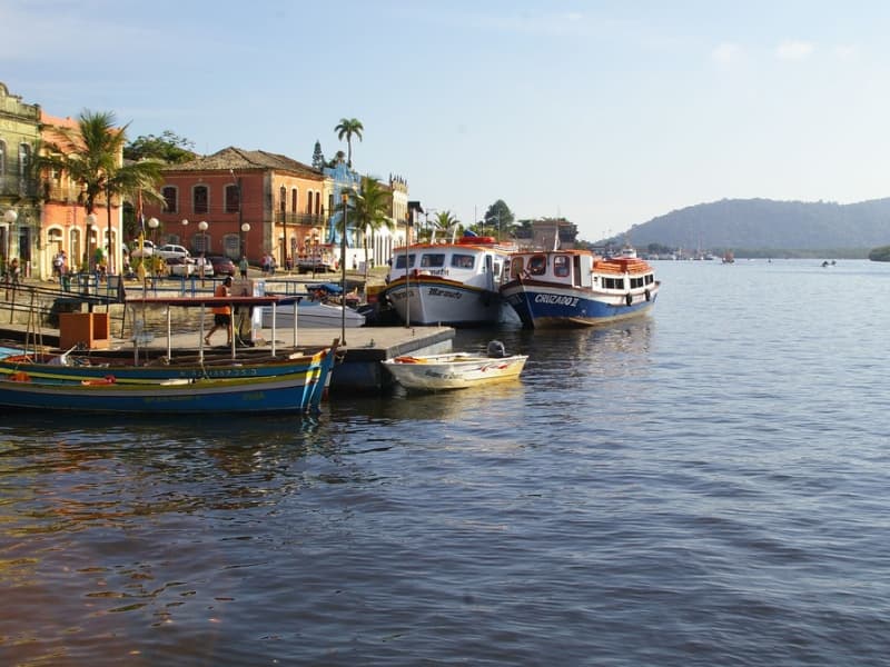 Trapiche municipal com embarcações ancoradas, casario colorido e montanhas
