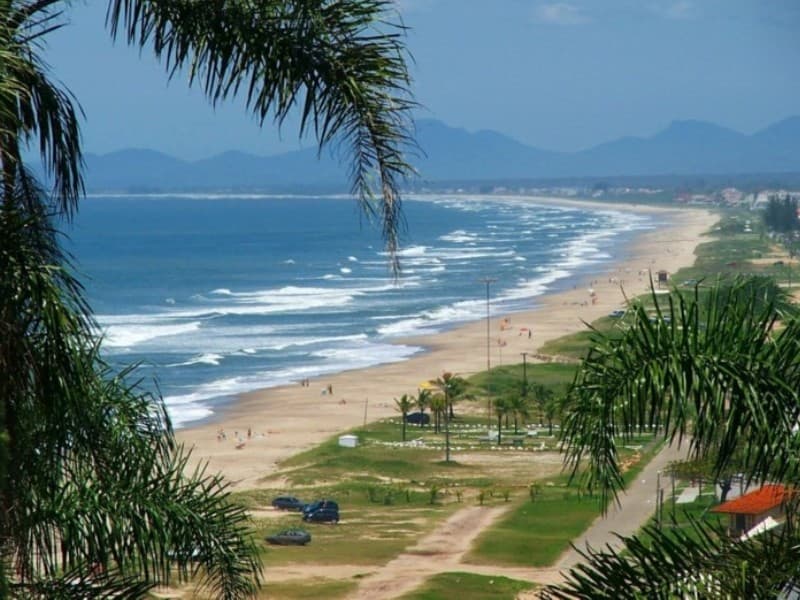 Praia extensa com ondas e palmeiras nos balneários de Guaratuba