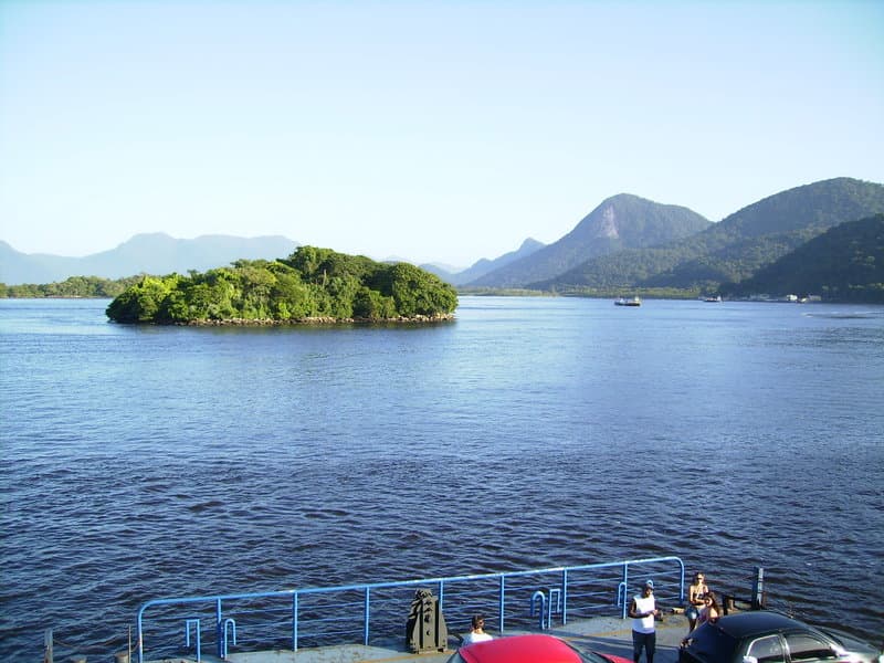 Foz da baía com ilha arborizada, águas calmas e montanhas distantes
