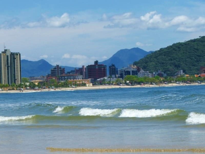 Praia Central de Guaratuba com mar calmo, orla urbana e montanhas ao fundo