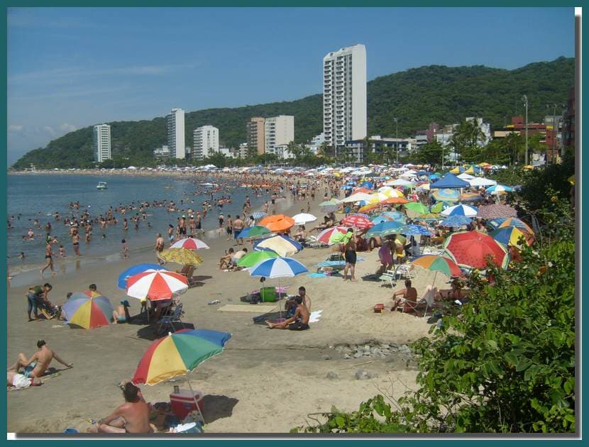 Praia Brava de Caiobá repleta de banhistas com guarda-sóis coloridos e edifícios à beira-mar