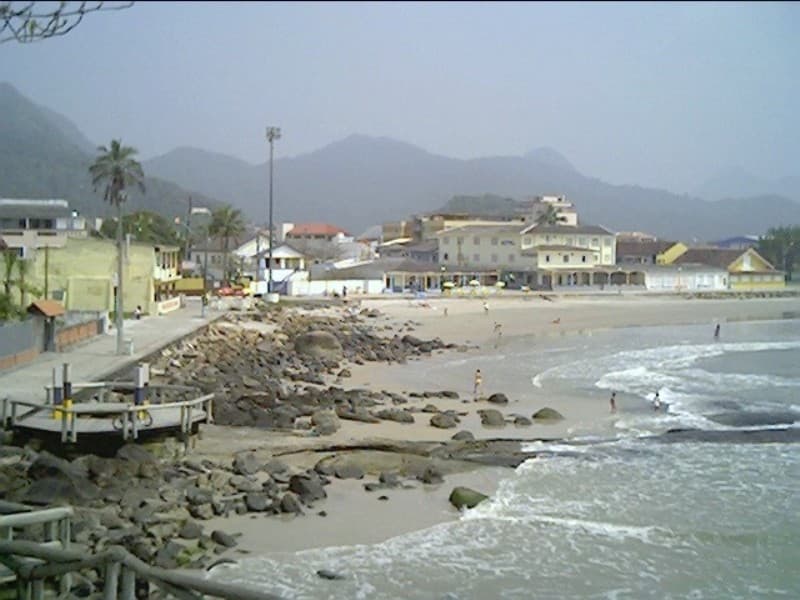 Orla marítima de Matinhos com faixa de areia, calçadão, mar e montanhas ao fundo