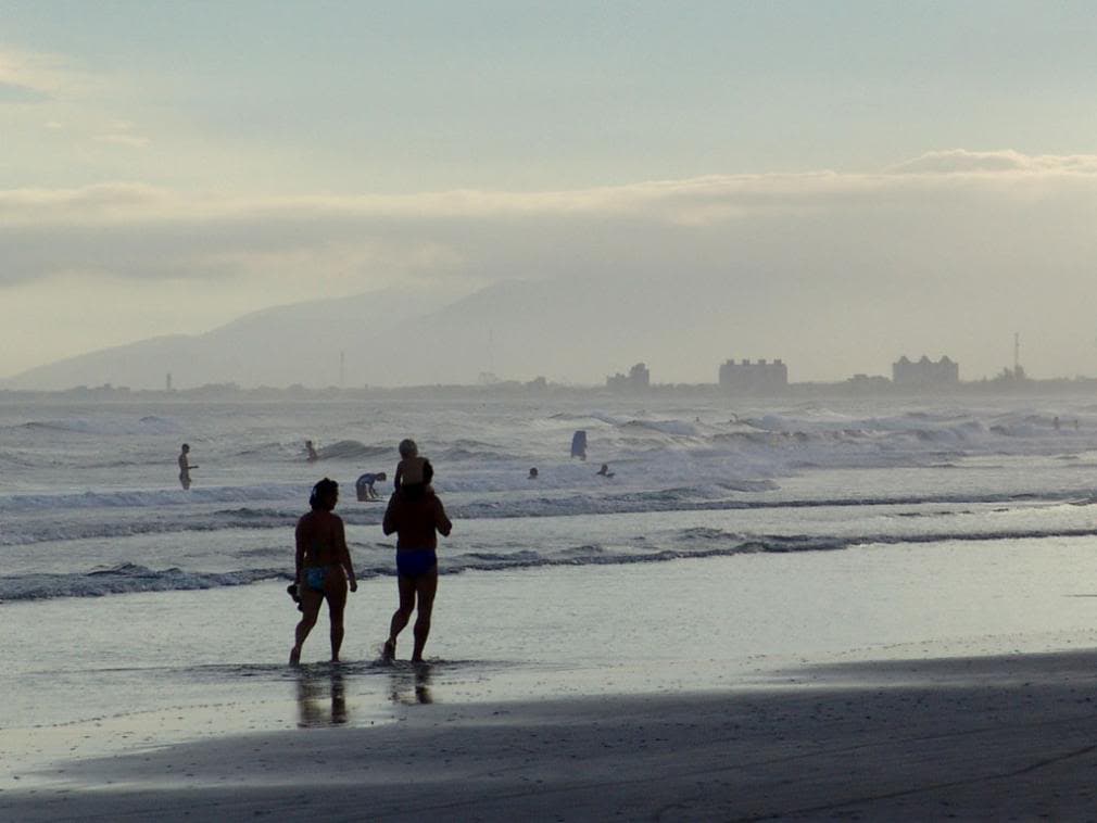 Banhistas caminhando na praia de mar aberto do Balneário Grajaú