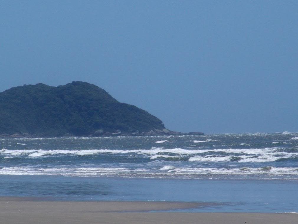 Praia arenosa com ondas e morro arborizado ao fundo em Santa Terezinha