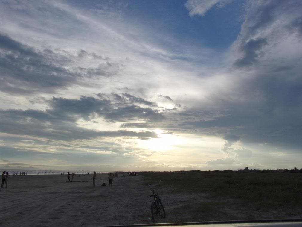 Praia ampla ao entardecer com vegetação de restinga e bicicleta na areia