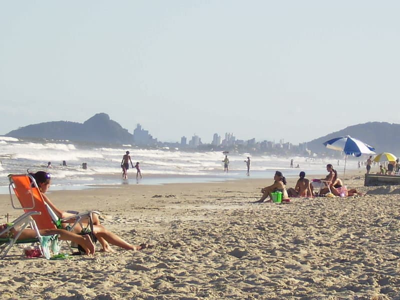 Praia de Leste movimentada com banhistas e edifícios à beira-mar sob sol