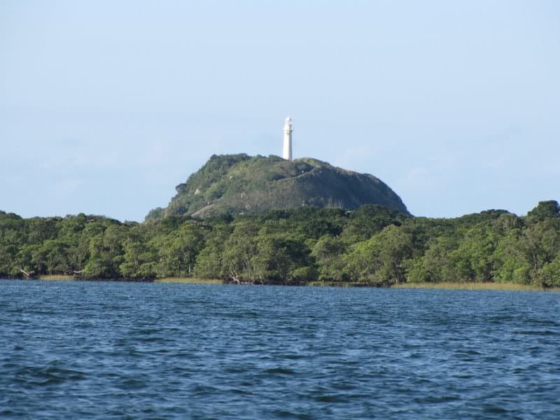 Morro verdejante com a torre branca do Farol das Conchas no topo da Ilha do Mel